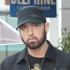 Eminem w czapce Kangol i czarnej kurtce. W tle tablica z napisem "BEEF MINE". Ciekawe, ile lat ma Eminem?